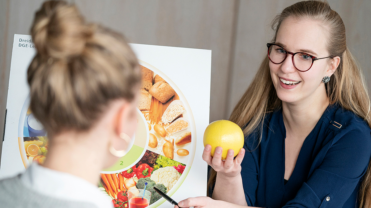 Bild Eine Frau erklärt einer anderen Frau anhand einer Ernährungstafel gesunde Ernährung